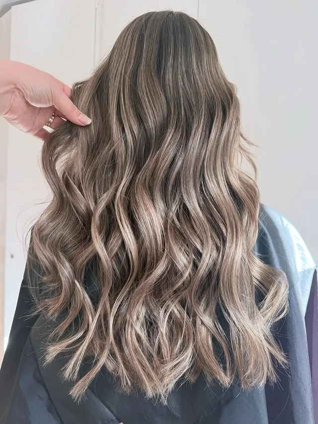 Balayage cendré beige sur cheveux longs ondulés
